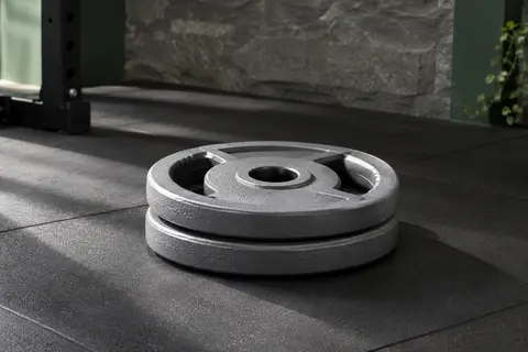 Paire de disques gris en fonte de 5 kg empilés dans un home gym, avec leur alésage central visible.