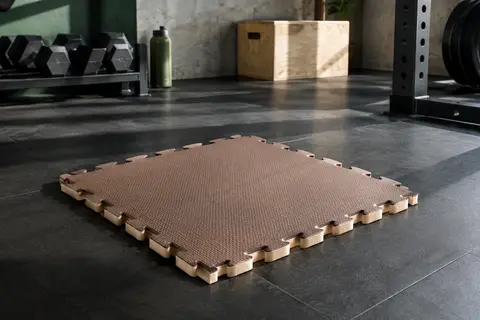 Dalle puzzle de protection en mousse EVA marron et beige, texturée et posée sur le sol d’un home gym