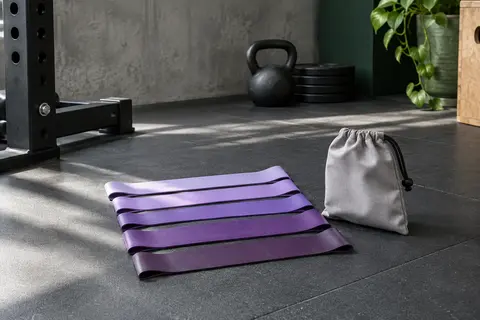 Lot de cinq bandes élastiques violettes en latex naturel avec sac de transport, posé dans un home gym sobre.