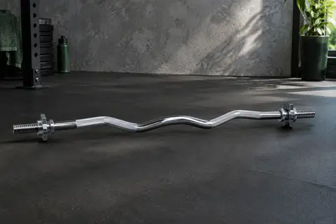 Barre curl chromée de 120 cm avec poignée antidérapante et fermetures à vis, dans un home gym.