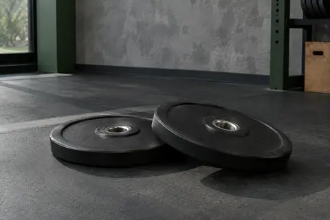 Paire de disques olympiques noirs caoutchoutés avec alésage central, posés dans un home gym sobre