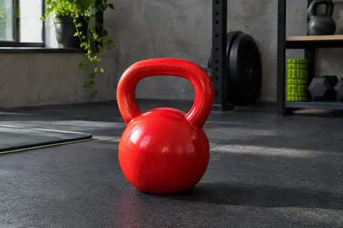 Kettlebell rouge de 8 kg en fonte avec revêtement vinyle, posée sur un sol sombre dans un home gym